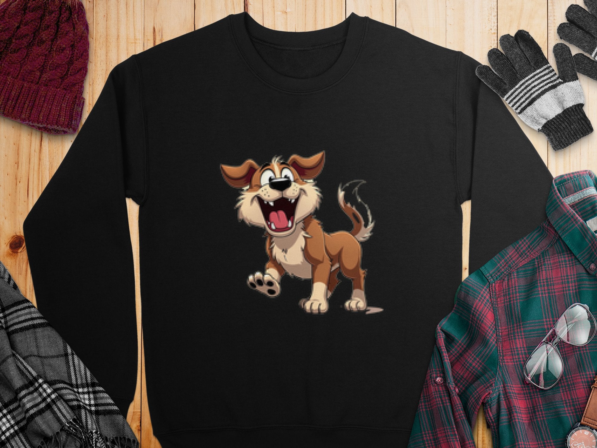 Garment Graphics presents a black sweatshirt featuring an animated happy dog with its tongue out, displayed on wood. Ideal for dog lovers, it’s paired with a red knit hat, gloves, plaid shirt, and checkered scarf.