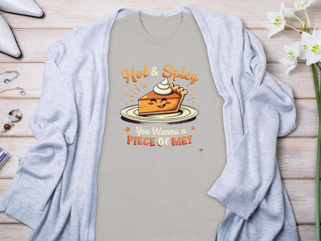 A light gray t-shirt from Garment Graphics featuring a cartoon pie slice with whipped cream and the text Hot & Spicy and You Wanna a Piece of Me? Its styled with a light blue cardigan, surrounded by white flowers, perfect for family sizing.