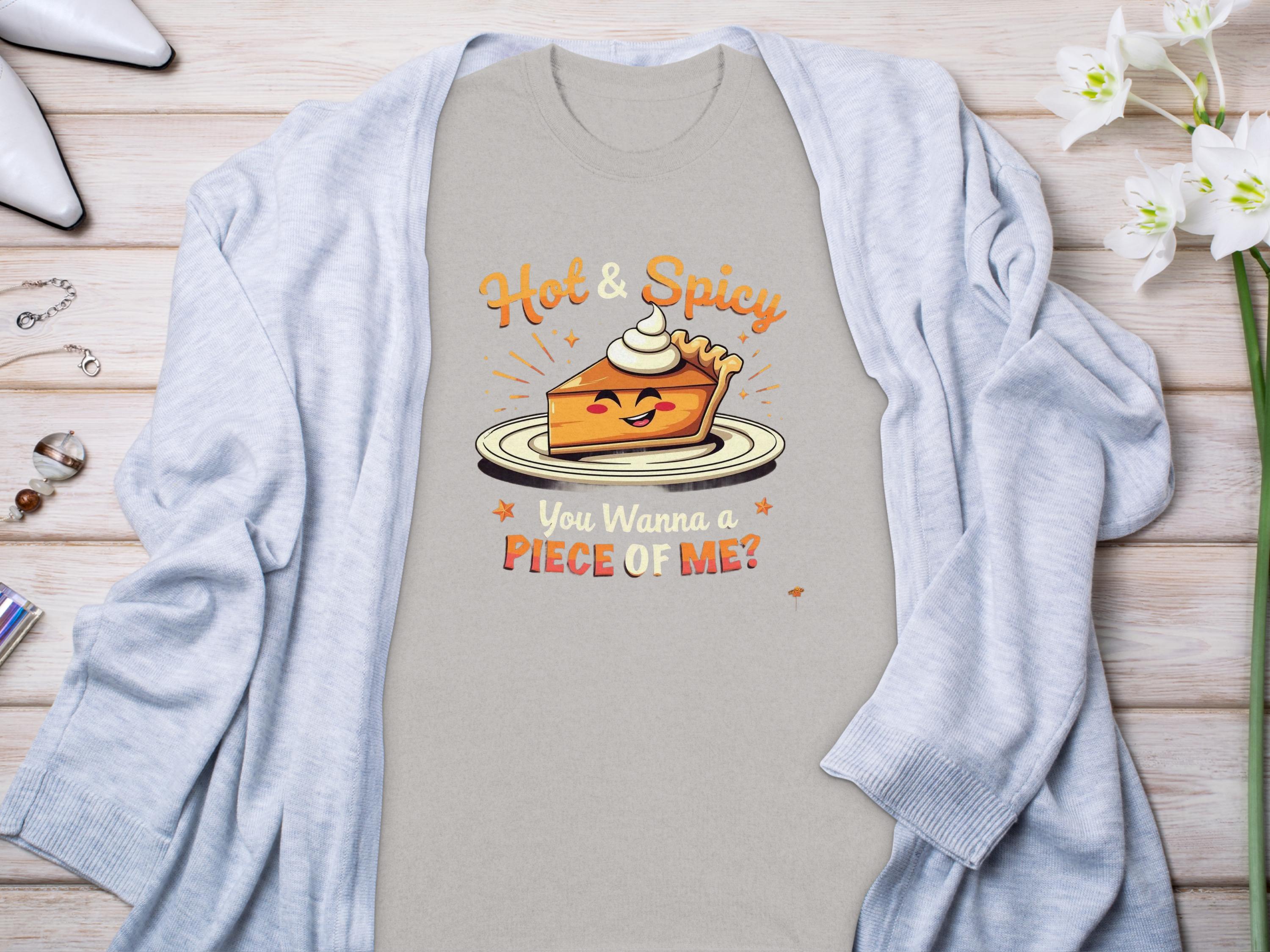 A light gray t-shirt from Garment Graphics featuring a cartoon pie slice with whipped cream and the text Hot & Spicy and You Wanna a Piece of Me? Its styled with a light blue cardigan, surrounded by white flowers, perfect for family sizing.