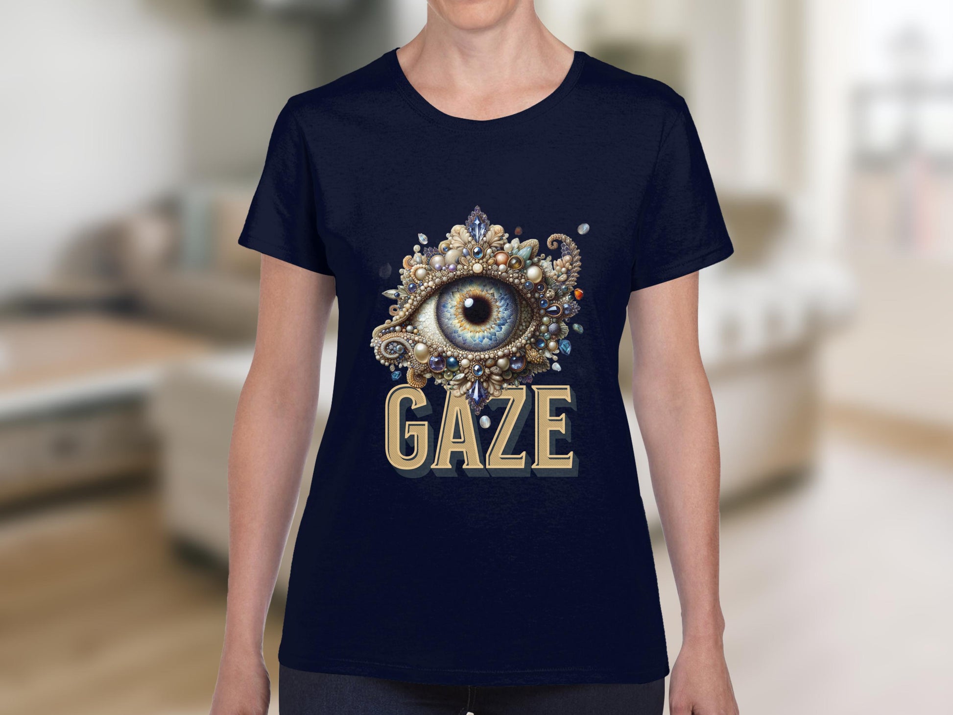 A person wearing a navy Garment Graphics T-shirt displays an ornate eye design with jewels and decorative elements, adding an artistic touch. GAZE is boldly printed below the eye. The softly blurred interior setting complements this unique piece in womens sizing.