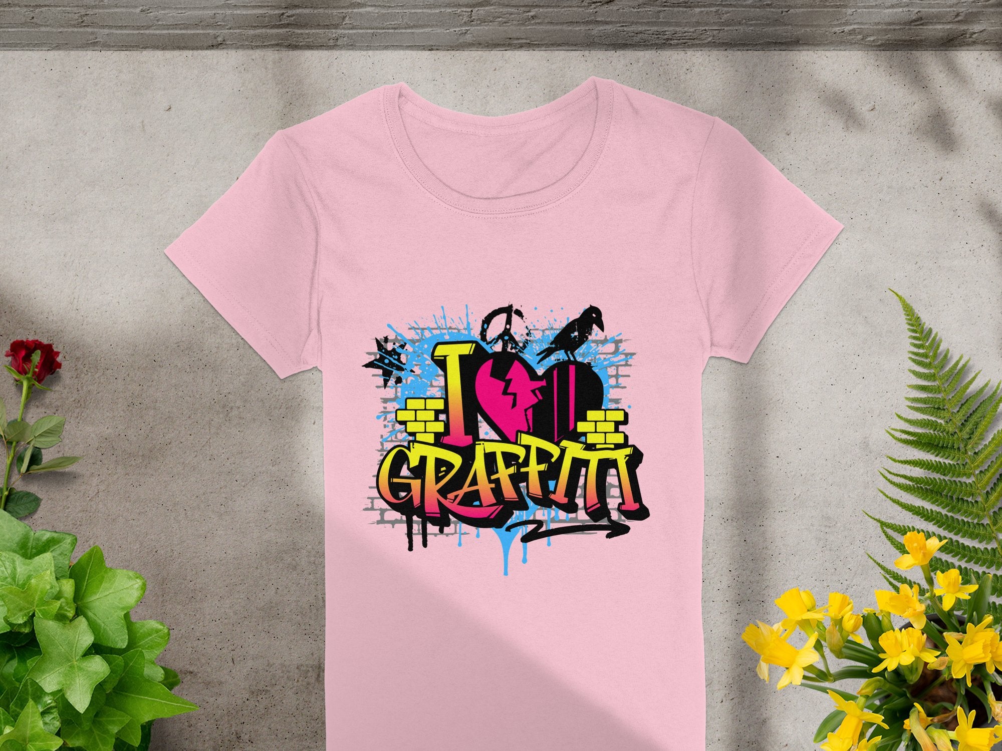 Garment Graphics pink T-shirt showcases street art with a vibrant I Love Graffiti design. Set against gray, it features a heart amid blue, yellow, and pink splashes framed by green and yellow plants, perfect for urban art fans.