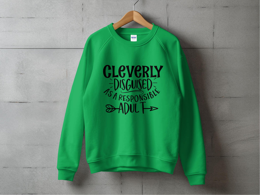A green Garment Graphics sweatshirt displayed on a wooden hanger against a concrete wall showcases black text saying Cleverly disguised as a responsible adult with decorative arrows. This humorous piece is available in unisex sizing for anyone ready to sport it.