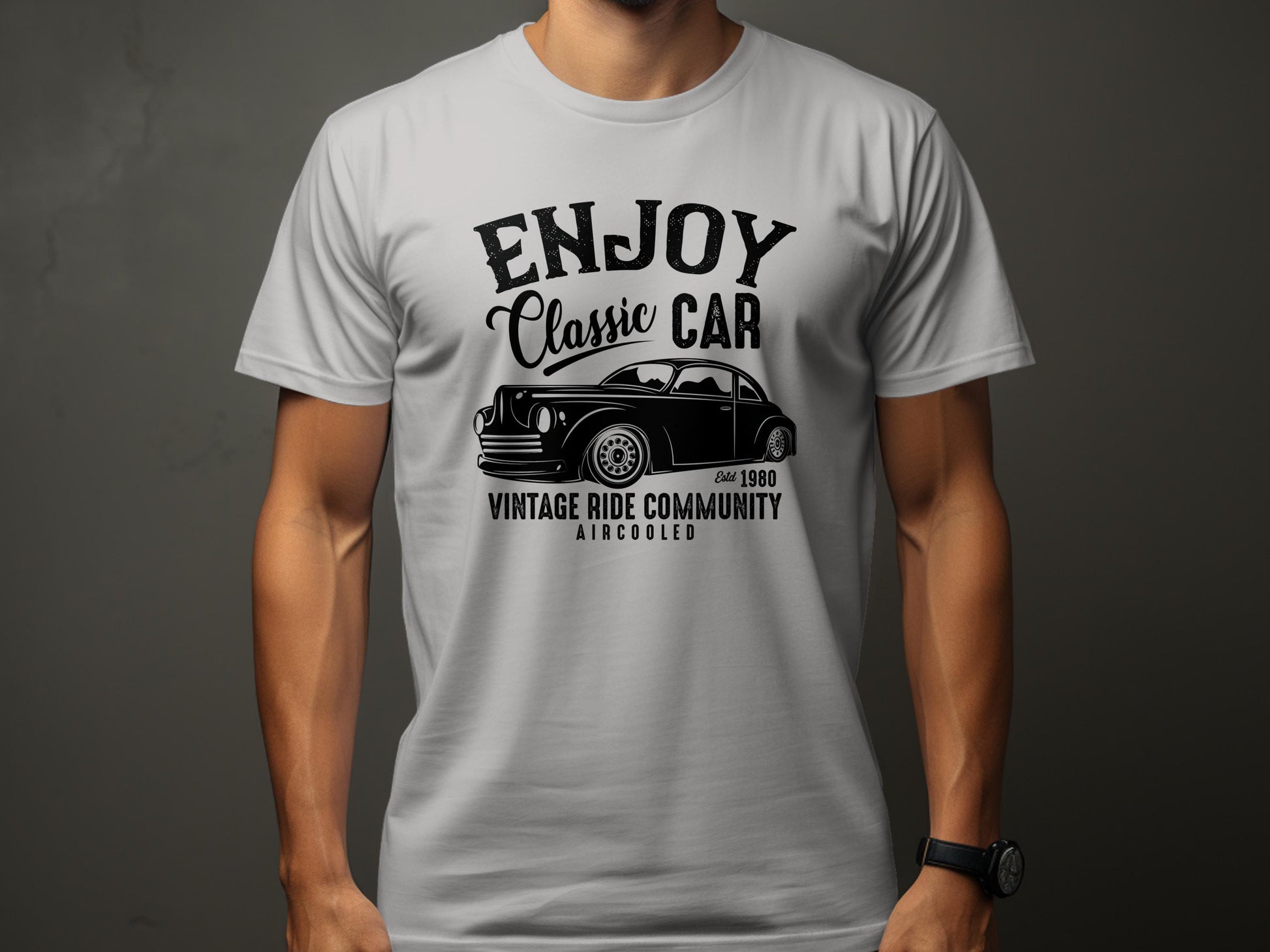 A man wears a light gray T-shirt by Garment Graphics, featuring a black classic car graphic and the text Enjoy Classic Car, Vintage Ride Community, Aircooled, Est. 1980, ideal for car enthusiasts.