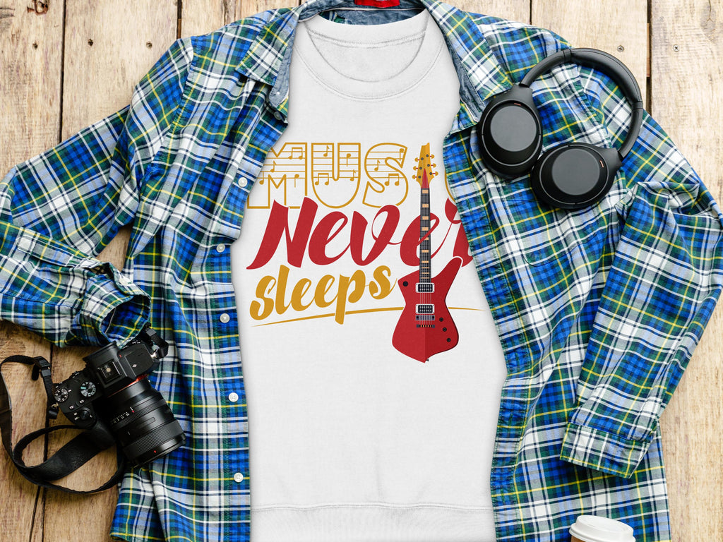 A flat lay photo features Garment Graphics plaid shirt, a vibrant Music Never Sleeps guitar-themed sweatshirt, over-ear headphones, a camera, and a coffee cup lid on wood—a perfect setup for music lovers.