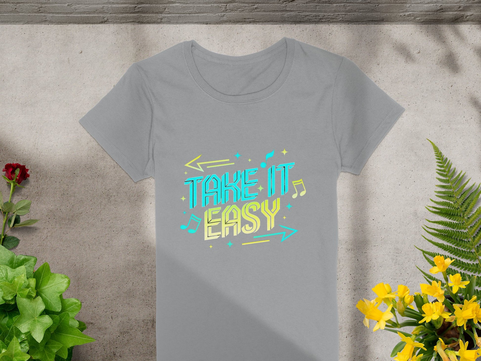Garment Graphics gray T-shirt boasts a chic design featuring TAKE IT EASY in vibrant yellow and blue with musical notes and arrows. Set against a stone backdrop, it’s enhanced by green plants, a red flower, yellow blooms, and dynamic shadows for extra flair.