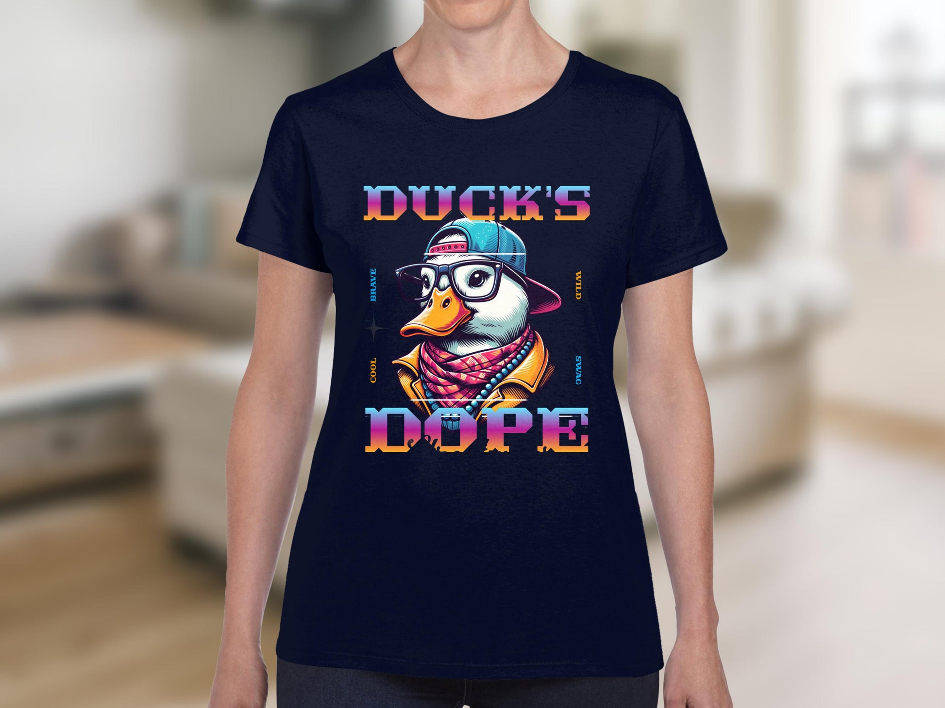 A person is wearing a navy blue Garment Graphics t-shirt featuring a duck with glasses, a blue cap, and a multicolored scarf. The words Ducks Dope frame the stylish duck. The background is a blurred indoor scene.