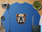 The Garment Graphics blue sweatshirt boasts a bold bulldog graphic with a spiked collar and is perfect for relaxed unisex wear. Its styled alongside items like a camera, lens, kiwi bowl, jute bag, book, and map on wood.