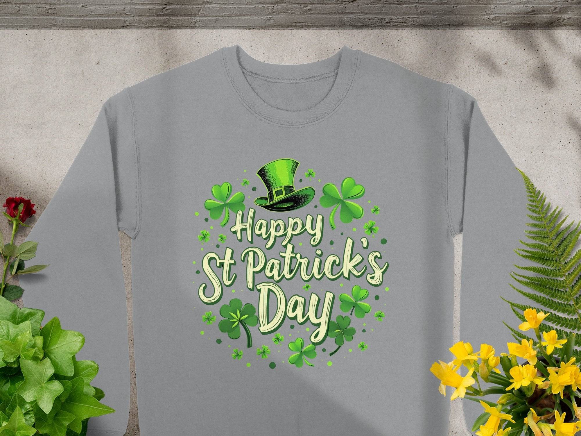 Garment Graphics presents a gray sweatshirt that exudes St. Patricks Day cheer with vibrant green Happy St Patricks Day print, shamrocks, and a jaunty top hat. Displayed on concrete, its paired with lush green plants and bright yellow flowers.