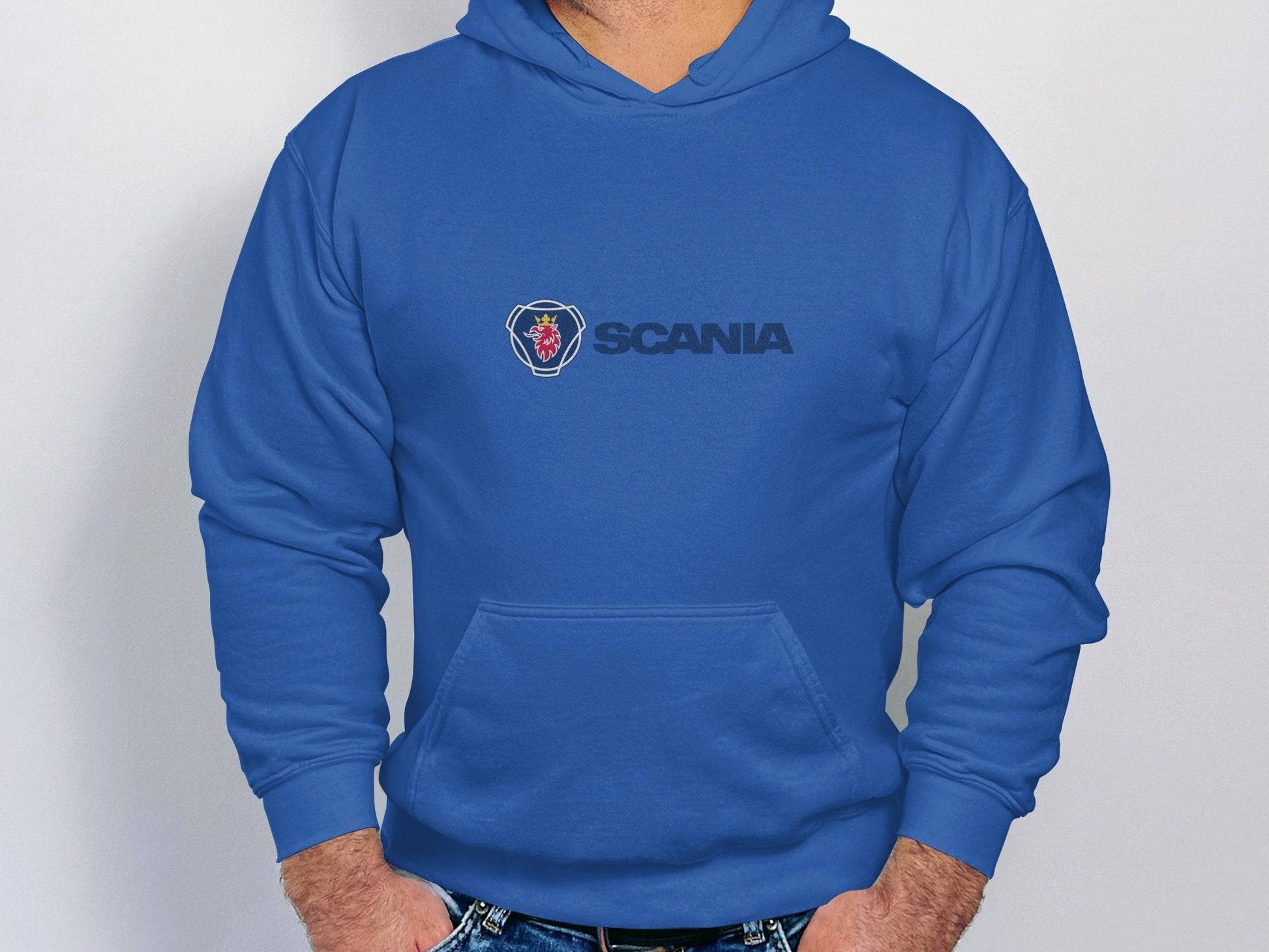 A person stands against a plain white background, wearing a Scania Hoodie by Garment Graphics. With hands in their hoodie pockets and paired with blue jeans, they exude a casual style that highlights unique fashion pieces.