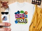 A white tee by Garment Graphics features Loud & Proud text in color, with blue fist, megaphone, star, and sports icons. Resting on wood beside a yellow jacket, pink shoes, and shades, this unique style matches the unisex fit of Loud and Proud sweatshirts seamlessly.