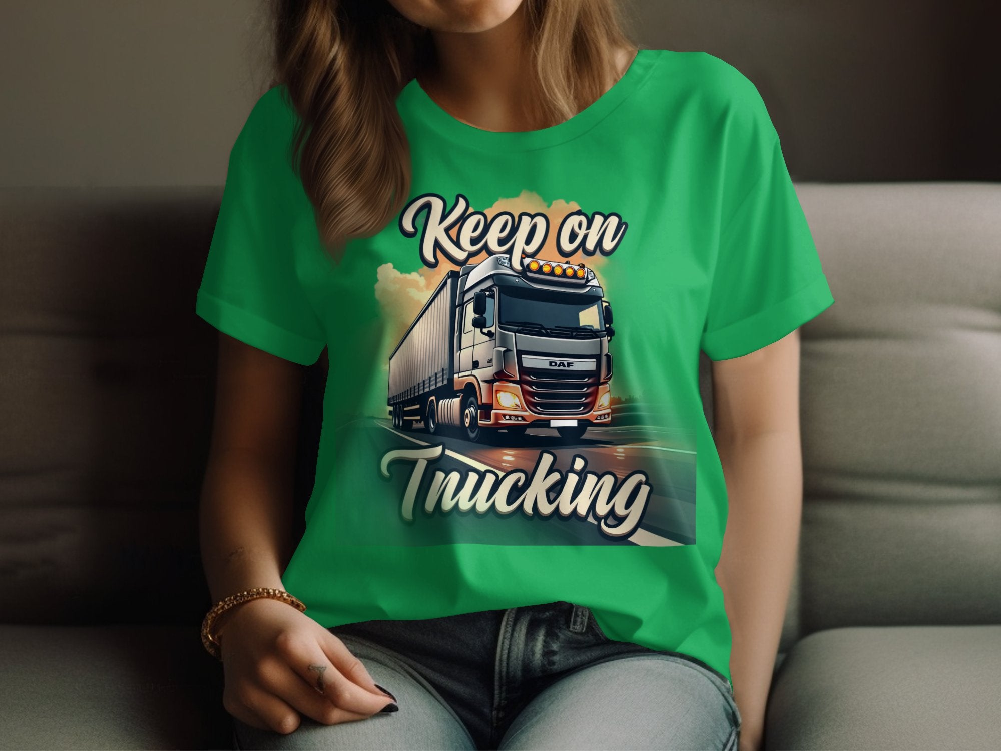 A person relaxes on a couch wearing a Garment Graphics green t-shirt featuring an illustrated powerful white truck with the text Keep on Trucking against a dynamic road background.