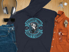 A Garment Graphics dark graphic hoodie with a Fishing Hair Dont Care fish slogan is displayed on wood, ideal for avid anglers. Its styled with headphones, sunglasses, jeans, a rust shirt, watch, keys, and glasses for an effortlessly cool vibe.