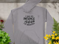 Garment Graphics gray hoodie features the text I had my patience tested Im negative in black, epitomizing funny statement hoodies. Its displayed on a concrete-textured surface, accented by red, yellow, and green plants.