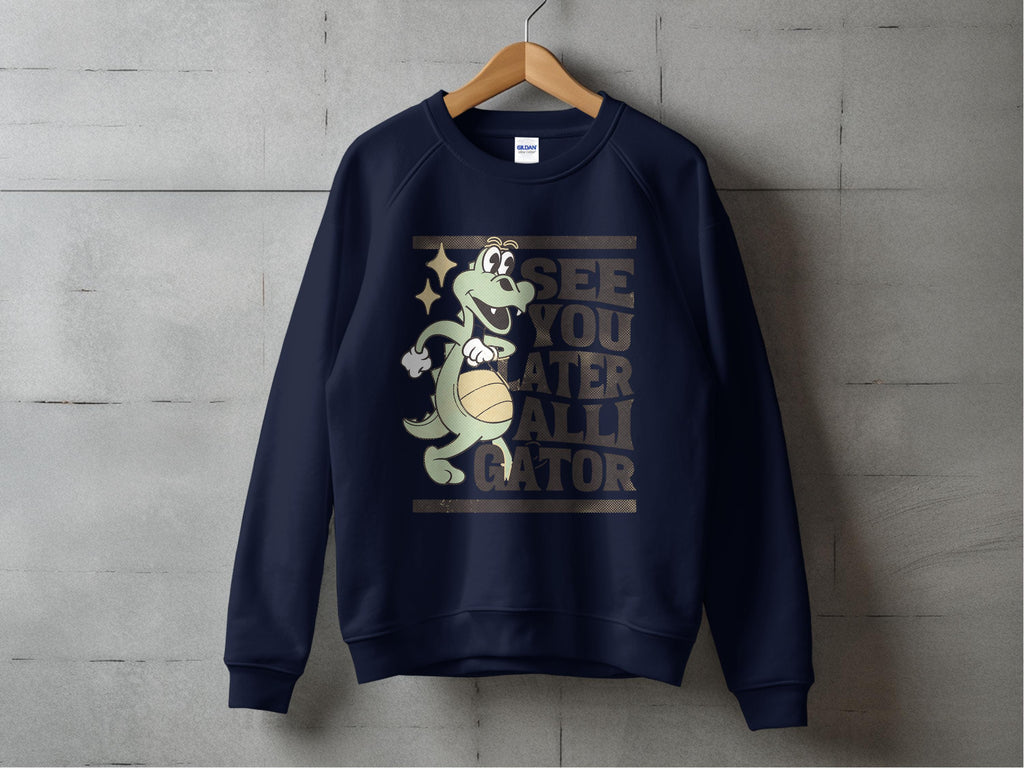 Garment Graphics navy blue unisex sweatshirt showcases a cartoon alligator with a beach ball and the caption, See you later alligator on the front. Displayed against a concrete wall backdrop.