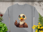 This cheerful cartoon eagle sweatshirt by Garment Graphics features a gray color, an eagle with glowing eyes giving a thumbs-up, set against lush green plants and small yellow flowers. Unisex sizing ensures style and comfort for all.