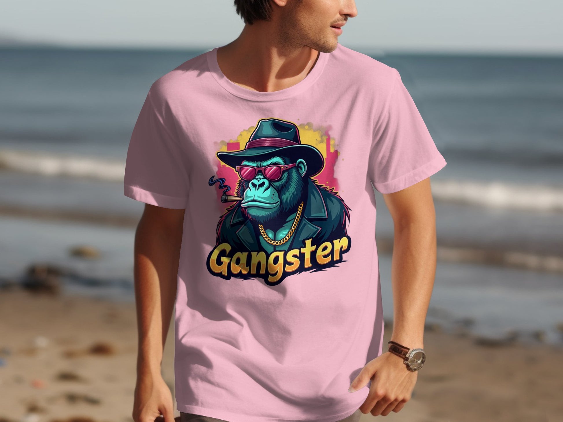 A man walks along the beach in a classic fit, urban style Garment Graphics pink T-shirt featuring a stylized chimp illustration wearing a hat, sunglasses, chain, and jacket with Gangster boldly printed below. The ocean backdrop highlights his Gangster Gorilla T-Shirt ensemble.