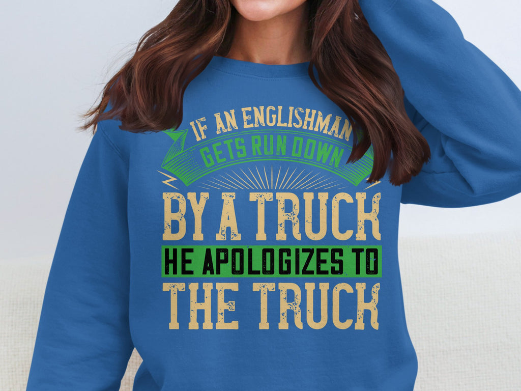 A person wears a Garment Graphics blue sweatshirt with a bold, humorous design: If an Englishman gets run down by a truck, he apologizes to the truck. The varying text colors—green, beige, black—add playfulness. Available in unisex sizing for everyone.