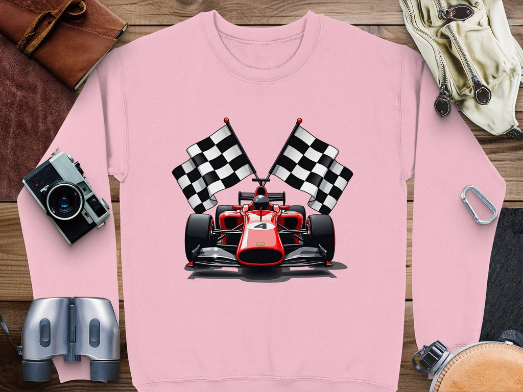 A vibrant pink sweatshirt from Garment Graphics, ideal for motorsport fans, is laid flat on a wooden surface. It showcases a red racing car with two black and white checkered flags. Surrounding it are items like a camera, binoculars, leather pouch, and goggles.