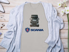 Truck enthusiasts will love this Garment Graphics gray t-shirt featuring a striking Scania truck and iconic logo. Styled on a light wooden surface, its paired with accessories, a light gray cardigan, and white flowers for the perfect look.