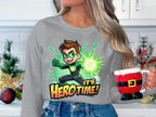In a festive kitchen, someone with long hair holds a Santa-themed mug and wears Garment Graphics unisex Its Hero Time! sweatshirt, showcasing a green cartoon superhero. Holiday decorations, including ornaments and berries, are visible in the background.