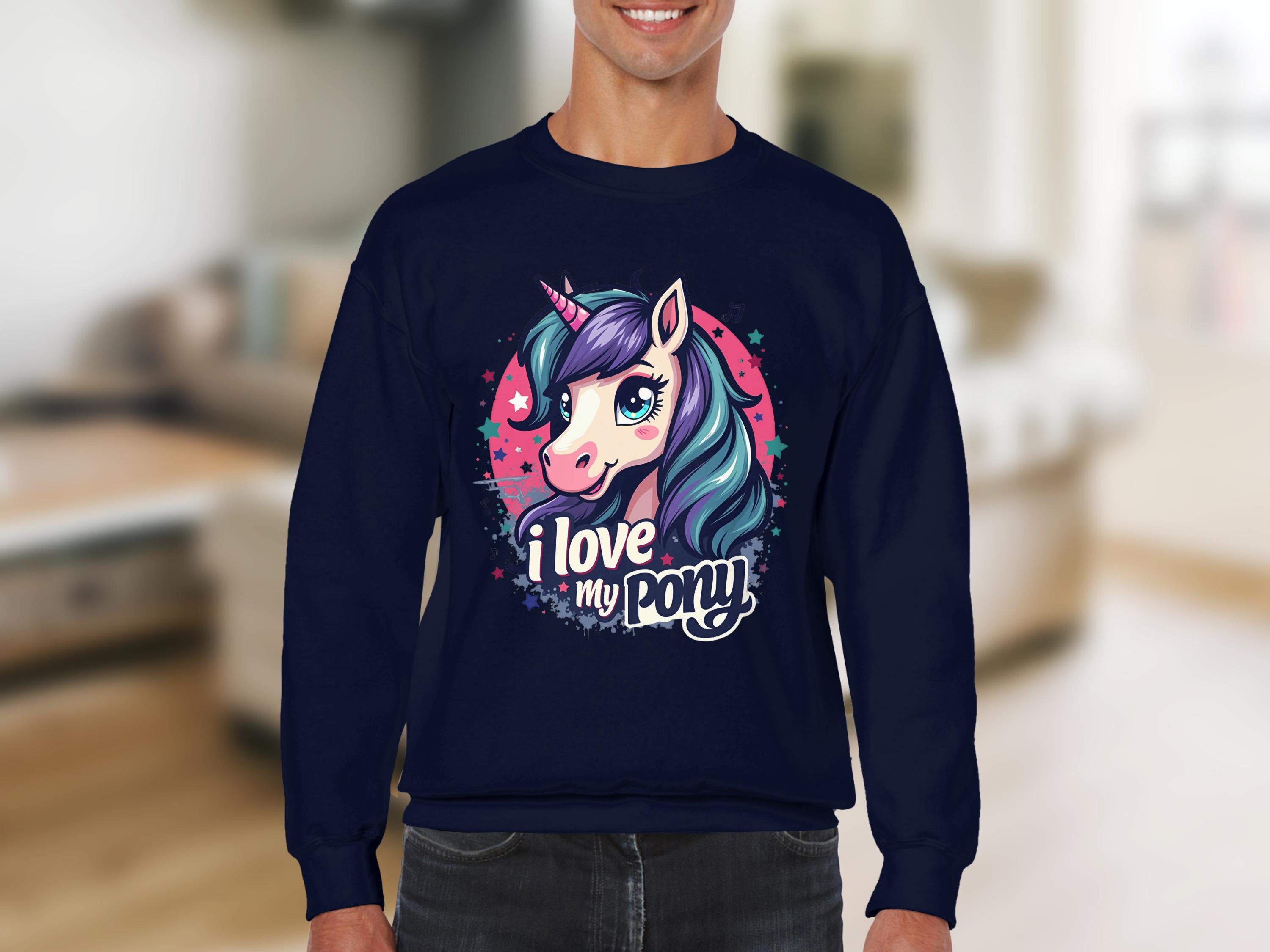 A person wears a Garment Graphics dark blue sweatshirt with a vibrant cartoon pony unicorn, featuring a blue mane and horn, and the words I love my pony. The softly focused room is the perfect backdrop for this whimsical attire.
