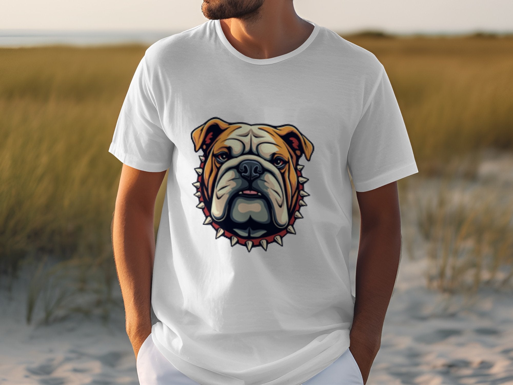 A person is wearing a trendy Garment Graphics T-shirt featuring a bulldog with a spiked collar design. Standing on a sandy path surrounded by tall grass, the focus is on this stylish shirt that effortlessly combines style and attitude.
