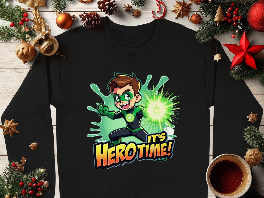 This Garment Graphics black shirt features a cartoon superhero with brown hair, a green mask, and costume holding a glowing orb, with the text Its Hero Time! Perfect for the festive season, this unisex graphic sweatshirt is styled among Christmas decorations and coffee on wood.
