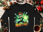 This Garment Graphics black shirt features a cartoon superhero with brown hair, a green mask, and costume holding a glowing orb, with the text Its Hero Time! Perfect for the festive season, this unisex graphic sweatshirt is styled among Christmas decorations and coffee on wood.