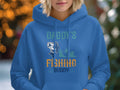 A person is wearing a blue hoodie from Garment Graphics Graphic Hoodies collection, featuring Daddys Fishing Buddy with fish and boat graphics. Softly blurred lights in the background suggest an ideal evening for outdoor adventures.