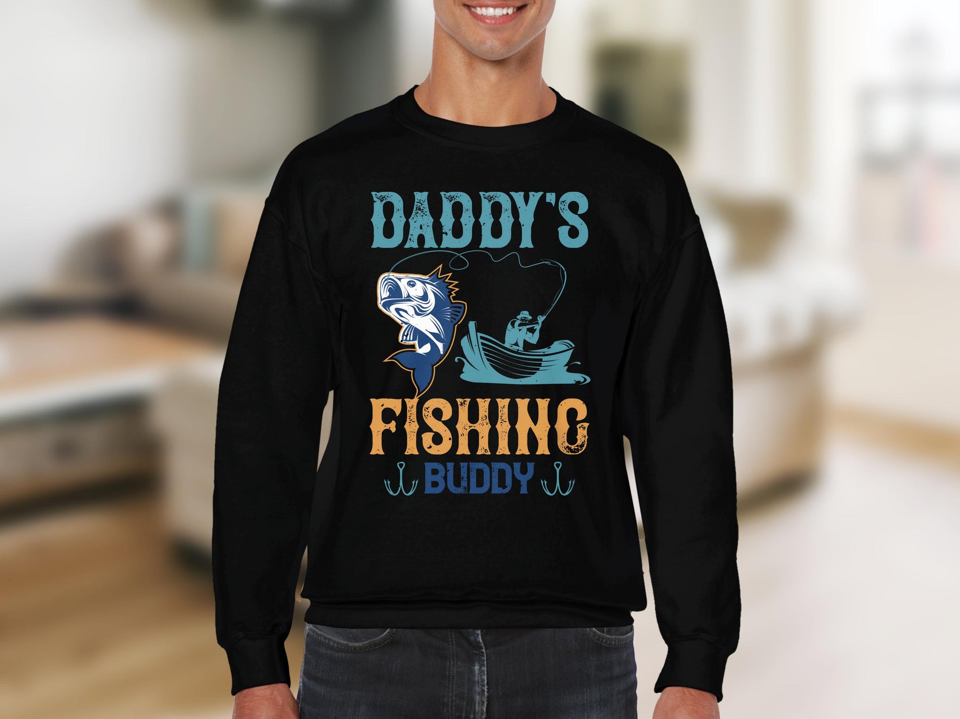 Someone is wearing a Garment Graphics sweatshirt with Daddys Fishing Buddy adorned with a cartoon fish and fishing scene. Ideal for outdoor lovers, the cozy setting highlights an indoor space with a blurred couch in the background.