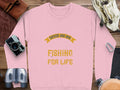 A pink Garment Graphics sweatshirt with Father and Son Fishing for Life in yellow is paired with a vintage camera, binoculars, brown shoes, a tan bag, and a sport cap.