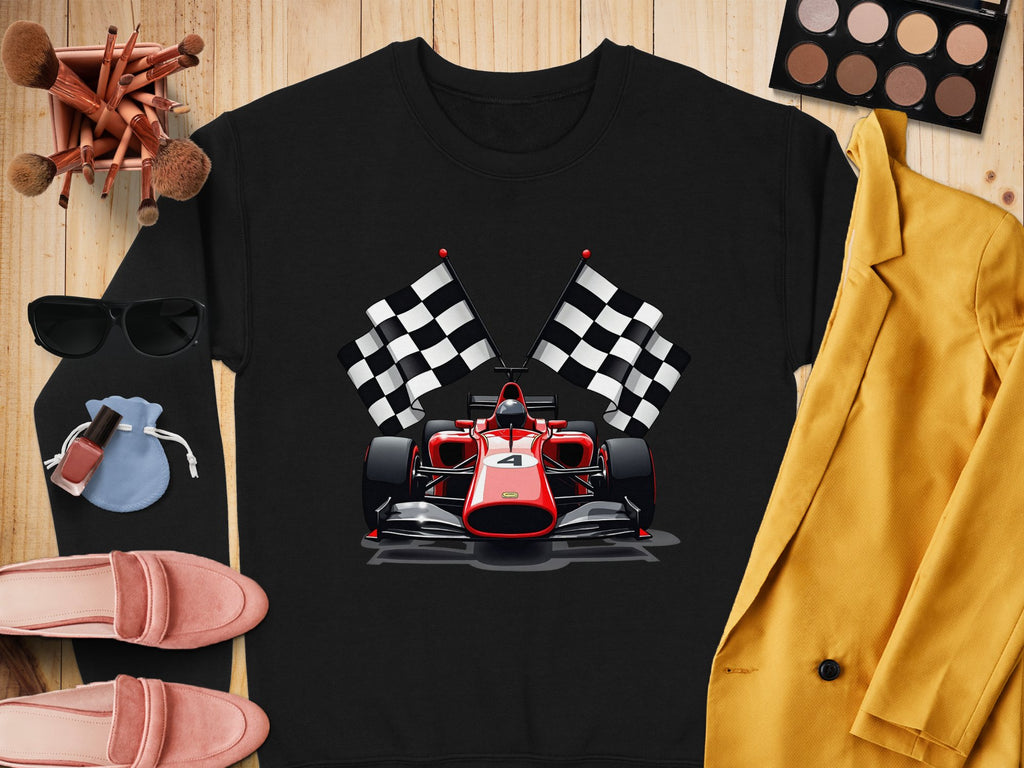A vibrant sweatshirt from Garment Graphics features a graphic of a red racing car and two checkered flags, ideal for motorsport fans. Surrounding it are makeup brushes, sunglasses, a blue pouch, yellow blazer, eyeshadow palette, lipstick, and pink loafers on wooden surface.
