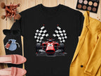 A vibrant sweatshirt from Garment Graphics features a graphic of a red racing car and two checkered flags, ideal for motorsport fans. Surrounding it are makeup brushes, sunglasses, a blue pouch, yellow blazer, eyeshadow palette, lipstick, and pink loafers on wooden surface.