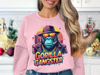 In an urban-style kitchen with holiday decor, a woman sports a pink Garment Graphics sweatshirt showing a gorilla in a suit, sunglasses, and hat. The bold text Gorilla Gangster under the image seamlessly merges fashion with flair.
