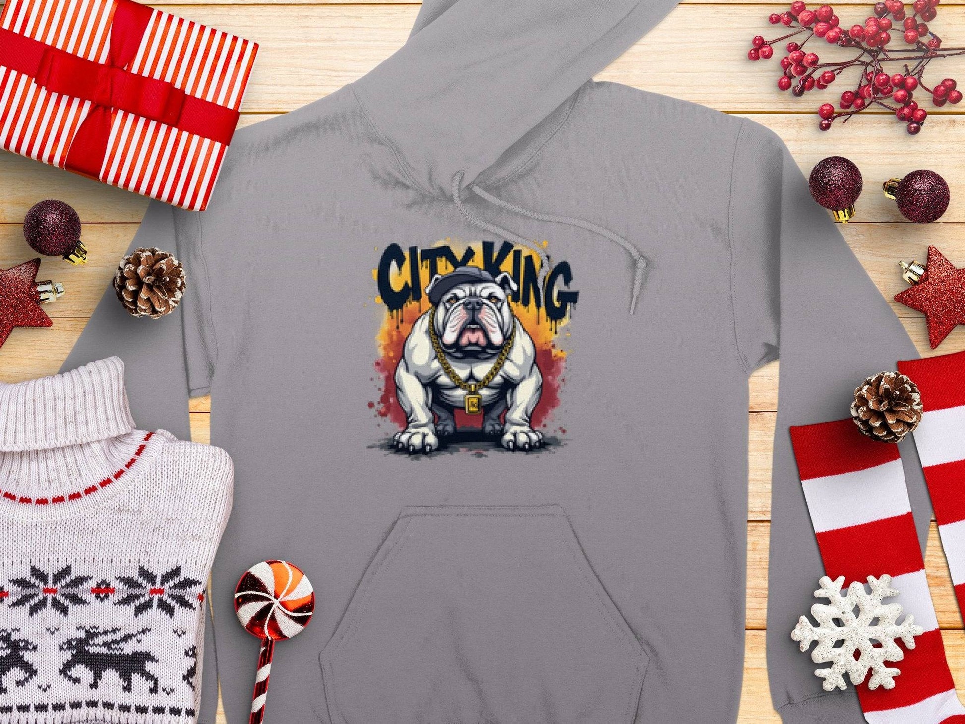 Garment Graphics presents a gray hoodie, ideal for casual wear, featuring a graphic bulldog with City King text. Displayed on wood with holiday décor like gifts and snowflakes, this Classic Fit piece combines style and comfort perfectly.