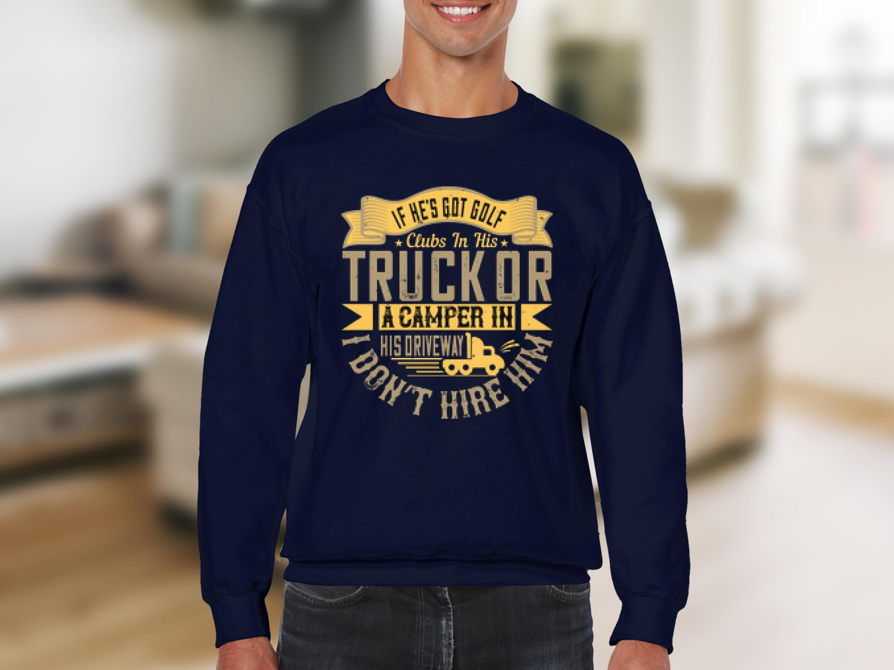 A person wears a Garment Graphics navy blue sweatshirt featuring a funny yellow text graphic: If hes got golf clubs in his truck or a camper in his driveway, I dont hire him, standing out against the blurred interior background.