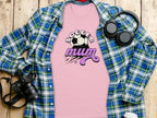 A flat lay showcases Garment Graphics classic fit Soccer Mum pink T-shirt with a soccer ball design, beneath an open blue and green plaid shirt. Nearby are headphones, a camera, and a disposable coffee cup on the wooden surface.