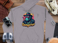 Garment Graphics gray hoodie features a cool ape illustration with a hat, sunglasses, jacket, and cigar. Gangster is emblazoned underneath. Made from medium-heavy fabric, its styled on wood with a camera and binoculars for the ultimate gangster gorilla graphic vibe.