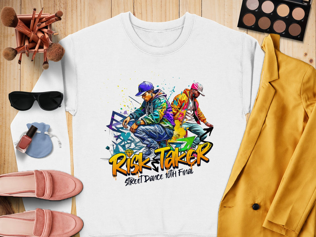 A white Garment Graphics t-shirt featuring two dancers with graffiti art and Risk Taker Street Dance 10th Final is displayed on a wooden surface. Its paired with a yellow blazer, pink loafers, black sunglasses, makeup essentials, a white watch, and a perfume bottle.