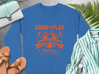 A blue football sweatshirt by Garment Graphics is displayed with an orange Born to Play and Young Squads Football soccer ball graphic. Nearby are a purse, sneakers, a striped shirt, and a fern leaf. It comes in unisex sizing for young squads.