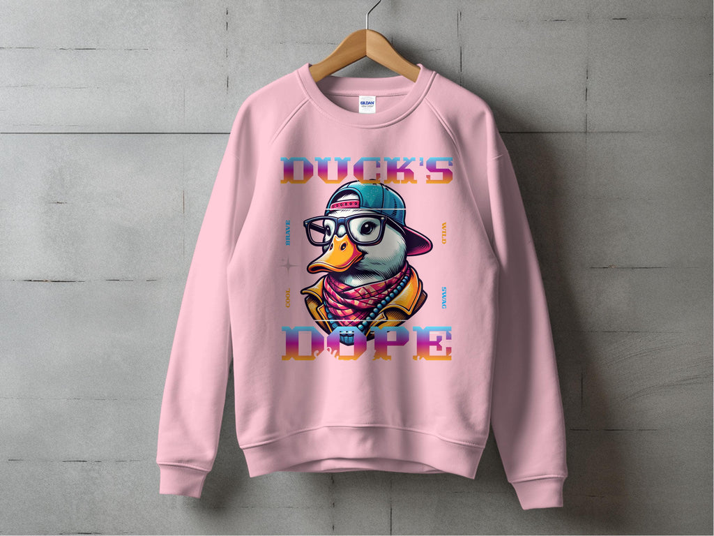 A pink Garment Graphics sweatshirt hangs against a concrete wall, displaying a cartoon duck with a baseball cap, glasses, and scarf. DUCKS DOPE is in bold colors on this unisex, medium-heavy fabric sweatshirt for ultimate comfort and cool swag.