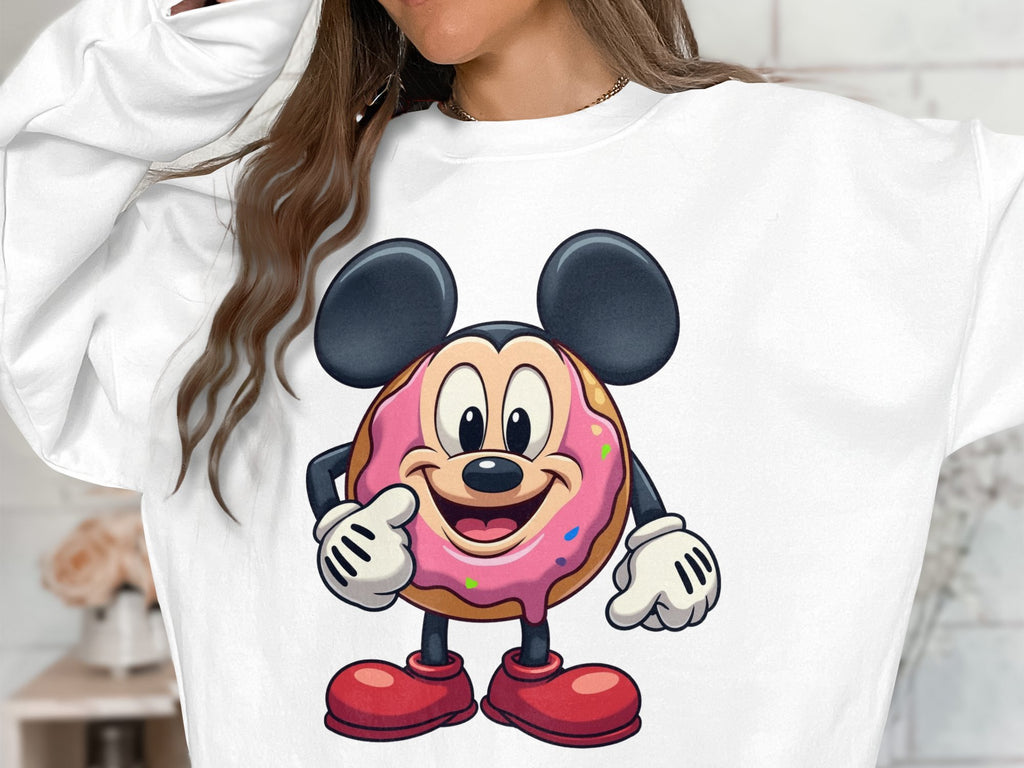 A person wears a Garment Graphics white sweatshirt with a playful donut character sporting mouse ears, shoes, pink icing, sprinkles, and offering a thumbs-up. This unisex design adds whimsical charm to any wardrobe.