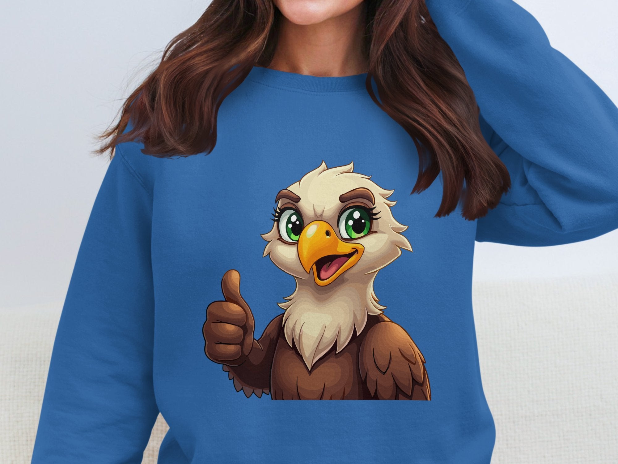 A person wearing a Garment Graphics unisex blue sweatshirt features a cartoon eagle with big eyes and a beak, cheerfully giving a thumbs up while hiding their face.