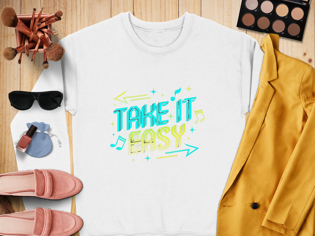 The Garment Graphics white shirt showcases a vibrant Take It Easy graphic with arrows and music notes. Ideal for pairing with a yellow blazer, pink shoes, sunglasses, makeup brushes, eyeshadow palette, and nail polish on wood for the perfect casual look.