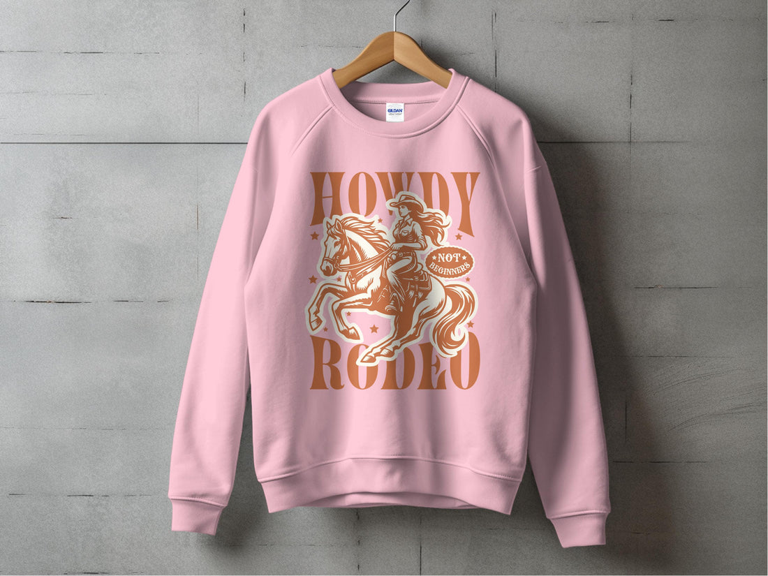 A person is wearing a Garment Graphics unisex graphic print sweatshirt featuring an illustrated cowboy on horseback with the words Howdy Rodeo and Notorious. Snow-covered trees in the blurred background enhance its charm.