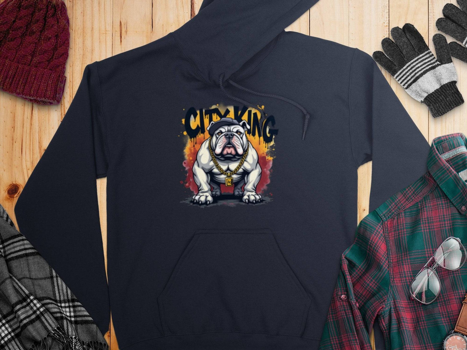 Garment Graphics presents a black hoodie with a bulldog design and CITY KING text for casual flair. Paired with a classic fit—a red knit hat, black and gray gloves, green and red plaid shirt, plus a black-and-white checked scarf—all set elegantly on a wooden surface.