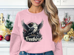 In a kitchen decorated for the holidays, a woman with long hair wears a pink sweatshirt adorned with an eagle design and Freebird from Garment Graphics, showcasing the casual appeal of their unisex Freebird graphic sweatshirts.