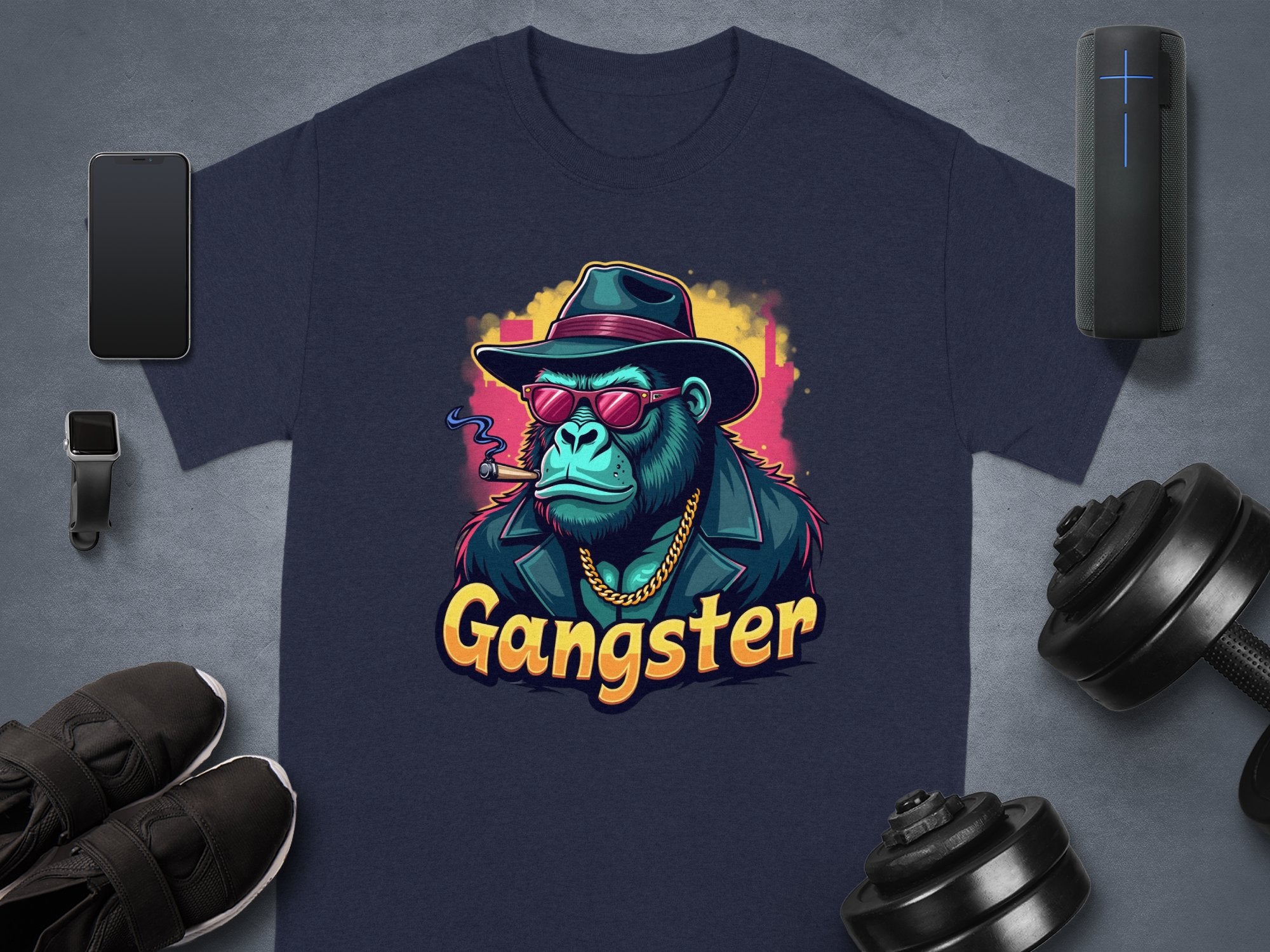 The Gangster Gorilla T-Shirt by Garment Graphics showcases a navy blue design with a gorilla in a fedora, sunglasses, leather jacket, and cigar. Gangster is boldly printed below. This urban classic fit pairs well with accessories like phones, smartwatches, shoes, dumbbells, etc.