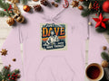 Garment Graphics presents a light pink medium-heavy hoodie with Just Dave Doing Dave Things, featuring a serene forest scene, festive Christmas details like pine branches, baubles, stars, and a cozy cup of coffee on a wooden surface.