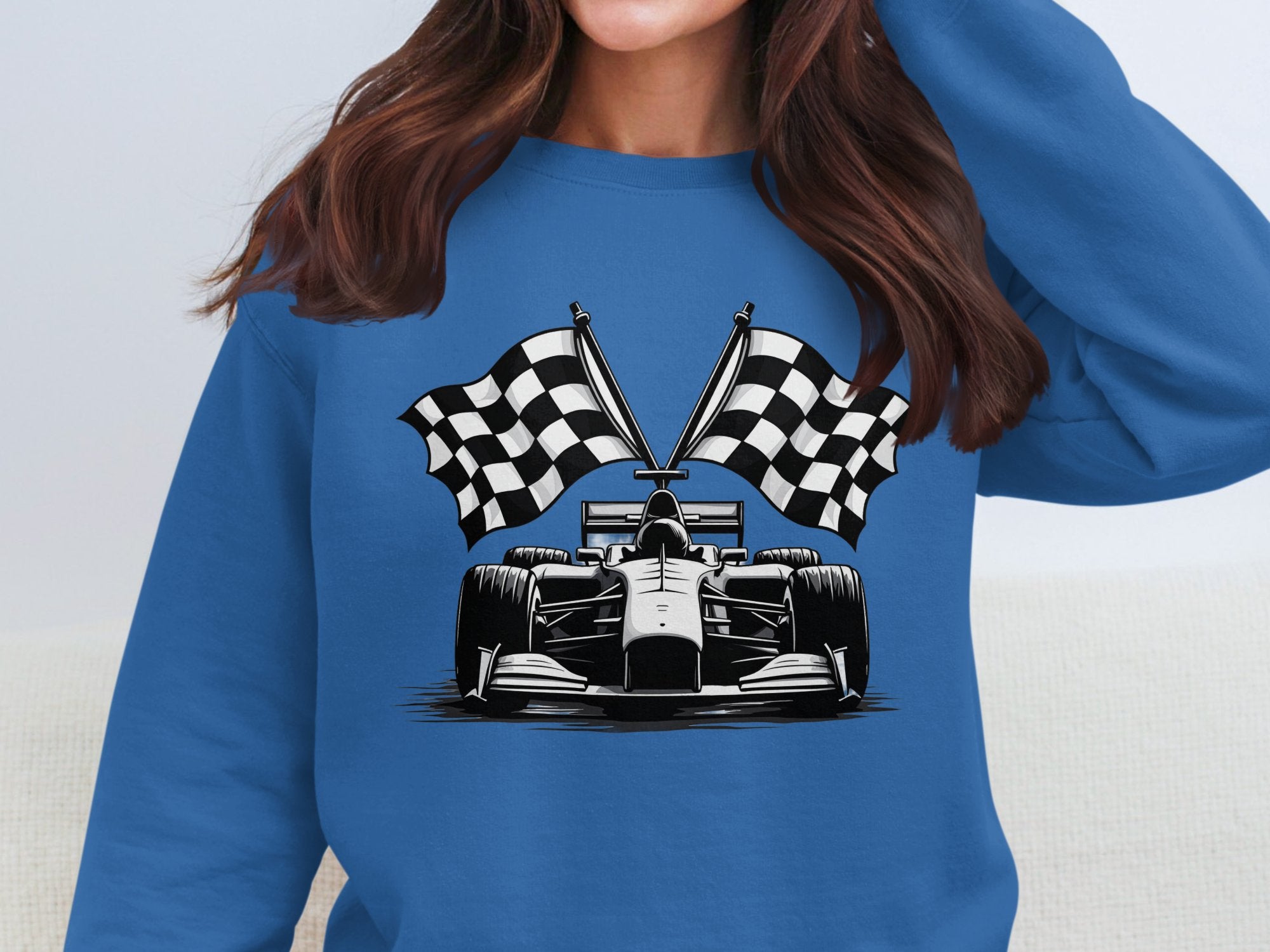 A woman wears a standout Garment Graphics racing car sweatshirt, showcasing a blue formula car graphic with crossed checkered flags. The eye-catching print draws attention, while her partially visible face adds mystery.